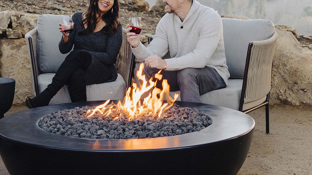 Couple sitting around outdoor fireplace enjoying wine at Jada Vineyard