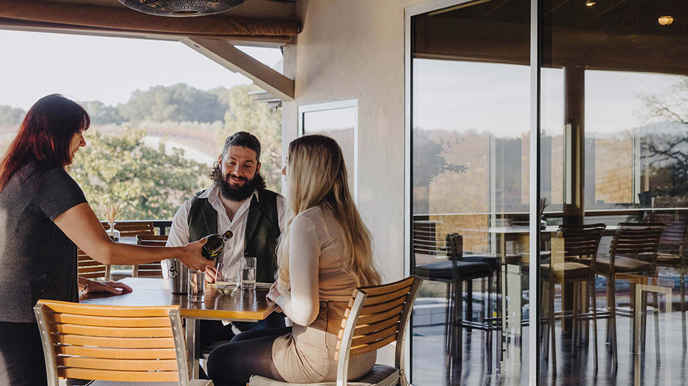 Waiter pouring wine for couple on Jada Vineyard Tree House deck